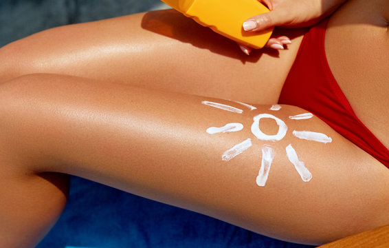 Young woman with sun shape on the leg holding sun cream bottle on the beach.Sunbath protection. Woman applying sunscreen on the beach.