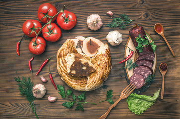 Sausage snag, pita bread, bagels, tomatoes, garlic, chilli pepper and greenery with fennels, dill and parsley on wooden table background.