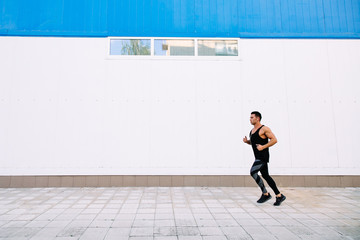 Fototapeta na wymiar Side view of portsman in black sportswear, during running outdoors. Healthy lifestyle.