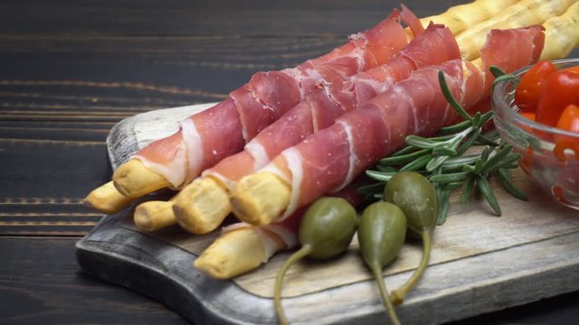 italian grissini with prosciutto, capers and pepper on wooden cutting board