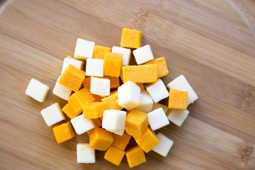 Pieces of mimolette and edam cheeses on wooden board, top view.