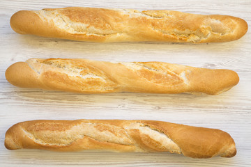 Fresh french baguettes on white wooden background, top view.