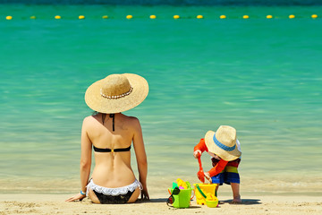 Two year old toddler playing with mother on beach