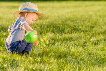 Toddler child outdoors. One year old baby boy wearing straw hat using watering can