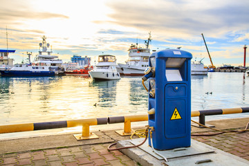 Fototapeta na wymiar Charging station for boats, electrical outlets to charge ships in harbor - supply electricity for recharging of battery on shore in marina jetty. Luxury yachts docked in port at sunset.