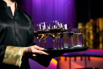 Waiter serving champagne and water on a tray. Waiter welcomes guests at the party in restaurant
