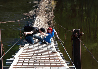 Naklejka premium The old bridge collapses over the river. A man helps a fallen woman and extends a hand.