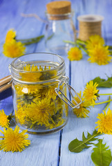 Vasetto di vetro con fiori di tarassaco e altri fiori e foglie sparsi © profumodarancia