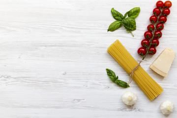 Pasta ingredients: spaghetti, cheese parmesan, garlic and tomatoes with basil on white wooden background, top view. Copy space.