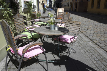 Tables in a street cafe decorated with pots with lobularia. White blankets on the backs of chairs