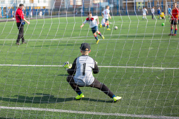 kid football goalkeeper jumps and catches a ball while training of his team on the stadium