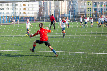 kid football goalkeeper jumps and catches a ball while training of his team on the stadium