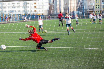 kid football goalkeeper jumps and catches a ball while training of his team on the stadium