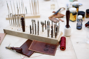 On the wooden table are a variety of tools for leather craft - 204693975
