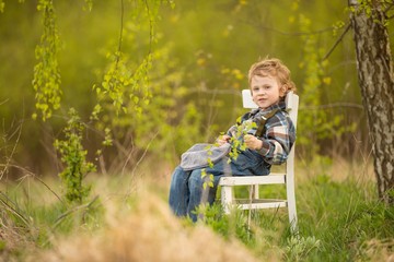 Young blonde boy relaxing on white old chair in spring landscape