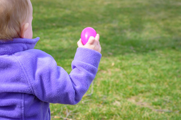 little girl holding up plastic Easter egg outside