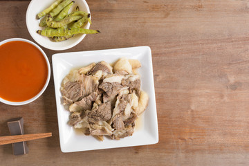 top view of sliced tender beef  served with spicy sauce and grilled chili on wooden table. asian style food concept.