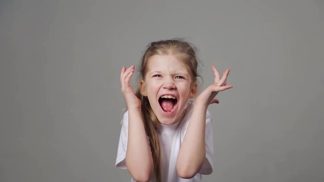 Pretty young girl shouting on grey background. Screaming child.