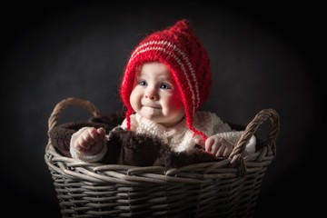 Beautiful baby girl sitting in basket, girl in red wool hat