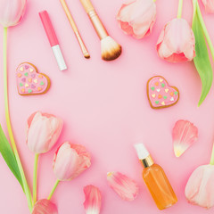 Frame with pink tulips flowers and cosmetics, cookies on pink pastel background. Flat lay, top view with copy space. Spring time