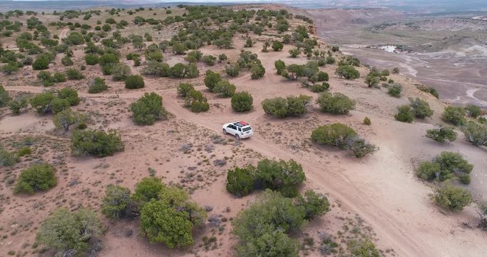 Aerial view of SUV car driving on a dirt road across a mesa covered by juniper trees - Westwater area in Utah
