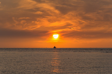 A ship at sea in the sunset with orange sky