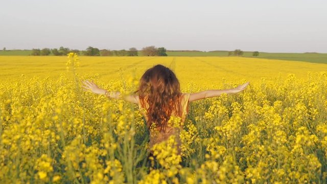 Child in the rapeseed field. Little girl on a field of yellow flowers. A happy child is running in the field.
