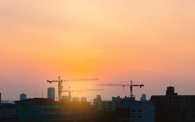 Fototapeta na wymiar silhouette view of urban infrastructure people property construction project with high cranes lifting in big city in morning skyline with sunrise golden hour.