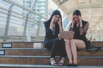 Fototapeta premium two business woman headache and stressed at outdoor sitting on concrete stair in city with using laptop checking about lose business planning project.