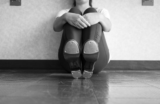 Black and White Version of Tap dancer sitting down, showing taps, and holding her legs