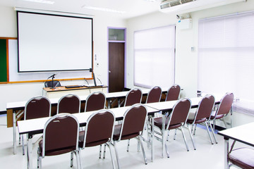 White classrooms are currently available with student desks and chairs. On the teacher's desk with stationery visualizer and microphone are located.