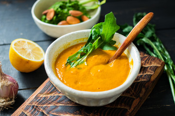 Yellow pumpkin avocado creamy soup dip in bowl with rocket salad, garlic, lemon on wooden board and dark background. Healthy organic farm ingredients product. Raw, vegan, vegetarian food
