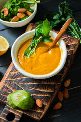 Yellow pumpkin avocado creamy soup dip in bowl with rocket salad, garlic, lemon on wooden board and dark background. Healthy organic farm ingredients product. Raw, vegan, vegetarian food