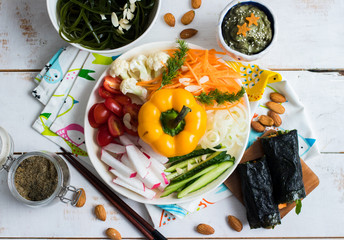 Raw vegan Buddha Bowl with vegetables. Capsicum, tomatoes, carrot, cauliflower, radish, cucumber, avocado dip suace, cabbage, seaweed salad, nuts, rolls. Top view. Vegetarian healthy food