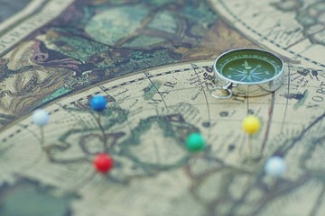 Compass and marking pins on blur vintage map, journey concept