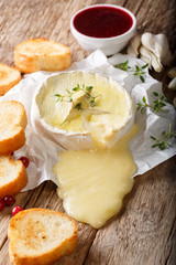 Delicious baked camembert cheese with thyme and garlic is served with toast and cranberry sauce close-up on the table. vertical