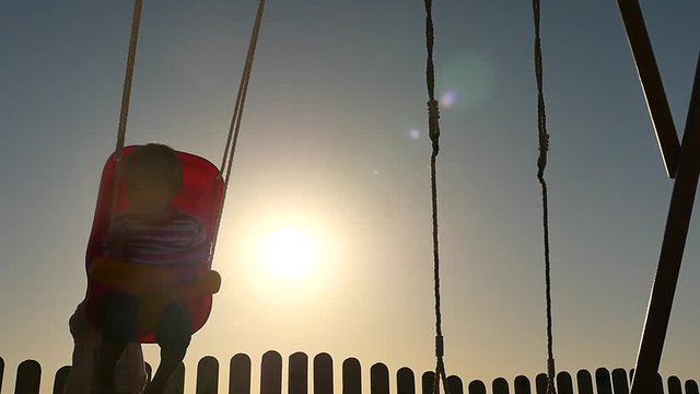 Happy Childhood concept - sister swing 1+ year old brother silhouette slow motion