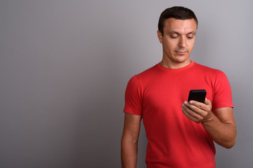 Man wearing red shirt while using mobile phone against gray back