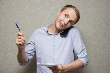 young guy in shirt talking on mobile phone with notepad and pen in hands