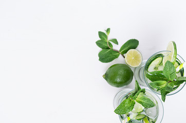 Fresh detox spring cocktail with mint, lime, ice, cucumber, straw as border on soft white wooden board, top view. Fun summer holiday background.