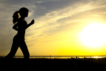 Fototapeta premium silhouette of a woman jogging on nature at sunset, sports female profile, concept of sport, leisure and healthcare