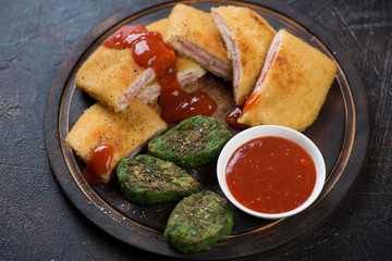 Sliced chicken cordon bleu with vegetable nuggets and sauce on a rustic wooden chopping board, horizontal shot
