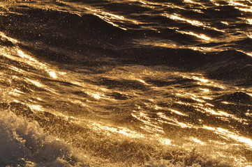 Turbulent water reflecting golden light of setting sun