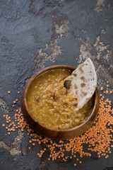 Wooden bowl of indian red lentil soup or masoor dal with chapati over brown stone background, vertical shot, copy space, elevated view