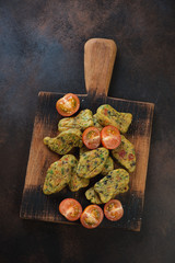 Wooden serving board with fried vegetable nuggets, flatlay on a brown metal background, vertical shot