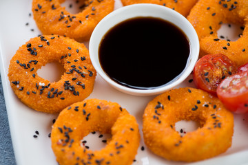 Close-up of fried breaded calamari rings with black sesame seeds and soy sauce, selective focus