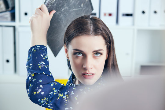 Angry business woman with folder trying to hit his colleague in office. Stressful situations at work.