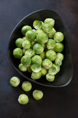 Black bowl with raw fresh brussels sprouts, top view on a brown metal background, vertical shot