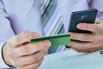 Man's hands holding a credit card and using smart phone for online shopping. Online payment