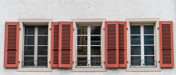 close up view of three windowls with wooden window shutters in red